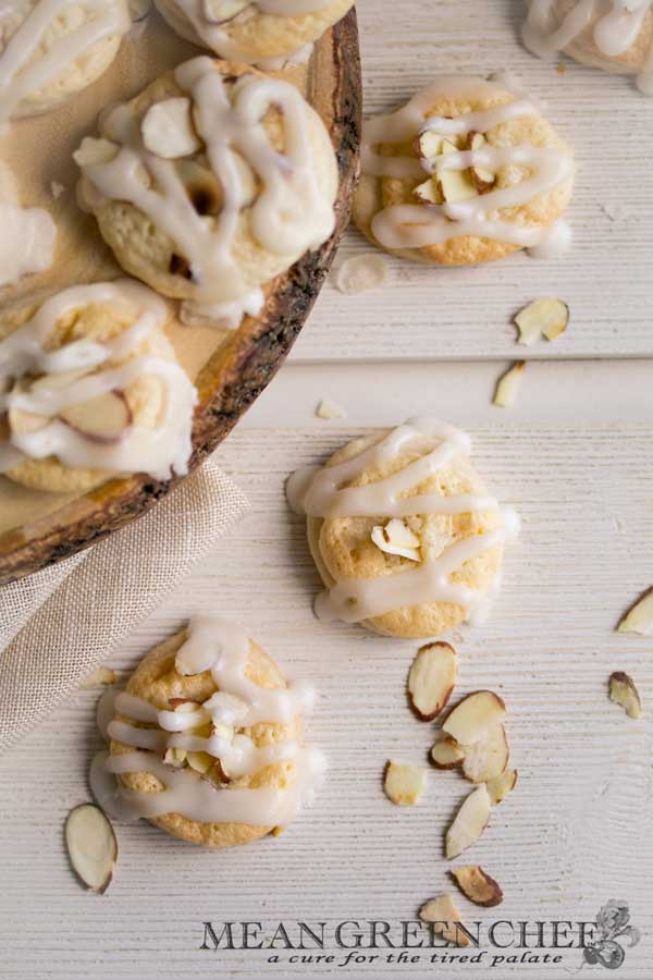 Overhead photo of Almond Pastry Cookies on white wooden background with roasted almonds sprinkled around.