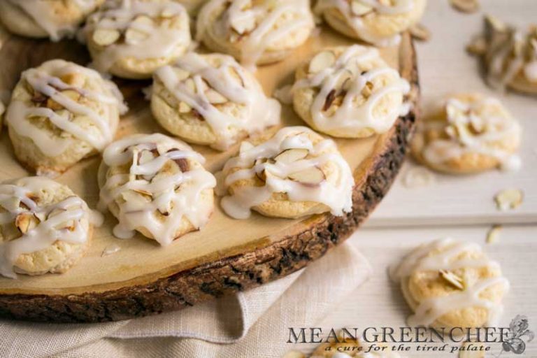 Overhead photo of Almond Pastry Cookies on white wooden background with roasted almonds sprinkled around.