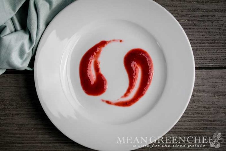 Fruit Coulis on a white plate sitting on a grey wooden background.