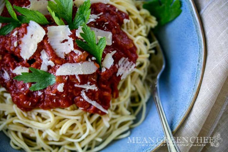 Overhead photo of homemade spaghetti topped with authentic red sauce garnished with parsley in a blue bowl.