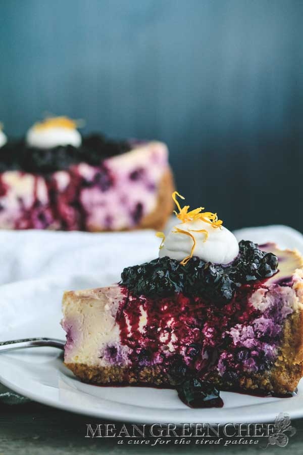 Side photo of a slice of Blueberry Lemon Cheesecake topped with blueberries and fresh whipped cream.