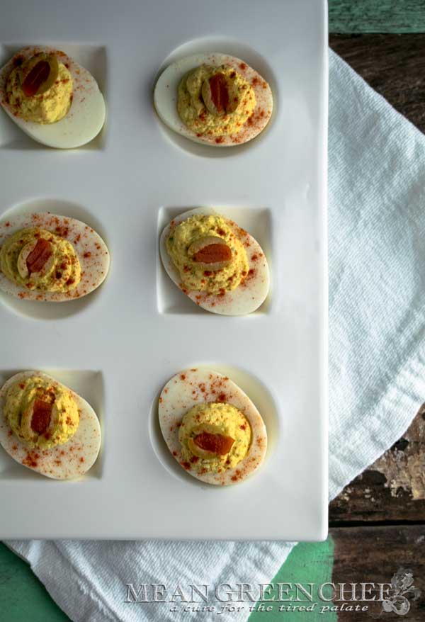 Classic Deviled Eggs on a large with platter with circle and square depressions for the eggs, sitting on a white cotton kitchen towel on an old blue wooden background. Mean Green Chef