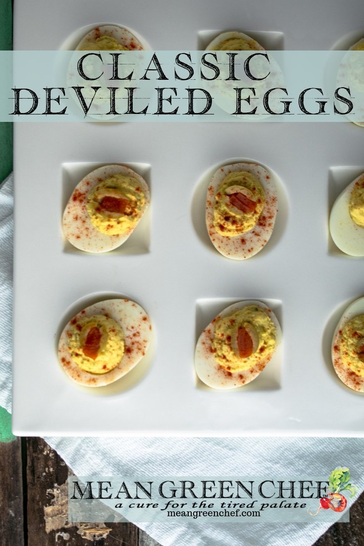 Classic Deviled Eggs on a large with platter with circle and square depressions for the eggs, sitting on a white cotton kitchen towel on an old blue wooden background. Mean Green Chef