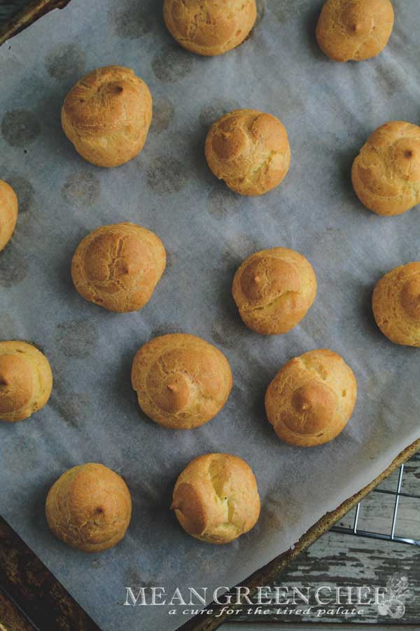 Pate a Choux Pastry baked to a golden brown sitting on a sheet pan lined with parchment paper.
