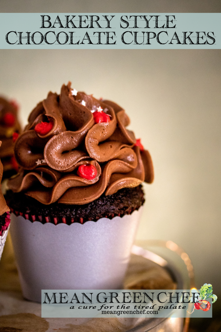 Side photo of Bakery Style Chocolate Cupcake decorated with a high swirl of chocolate frosting red frosting berries and a sprinkle of silver stars in a scalloped gray cupcake wrapper.