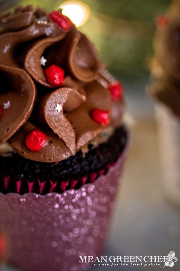 Side photo of Bakery Style Chocolate Cupcake decorated with a high swirl of chocolate frosting red frosting berries and a sprinkle of silver stars in a scalloped pink cupcake wrapper.