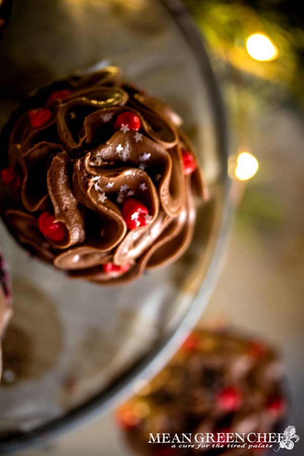 Overhead photo of Bakery Style Chocolate Cupcakes with high swirls of chocolate frosting that have been decorated with red frosting berries and a sprinkle of silver stars.