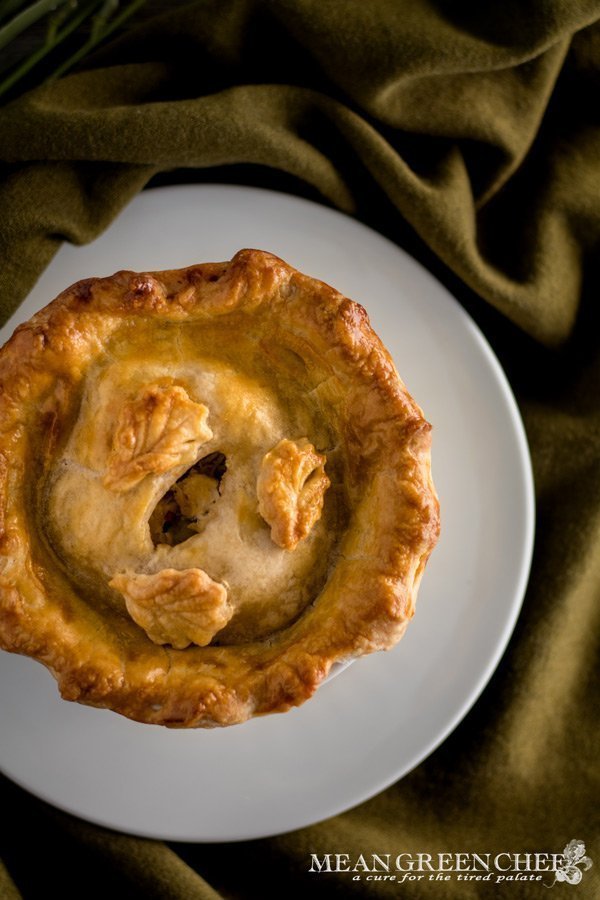 Overhead photo of a large double crust chicken pot pies in white ramekins on a green fabric background. Mean Green Chef
