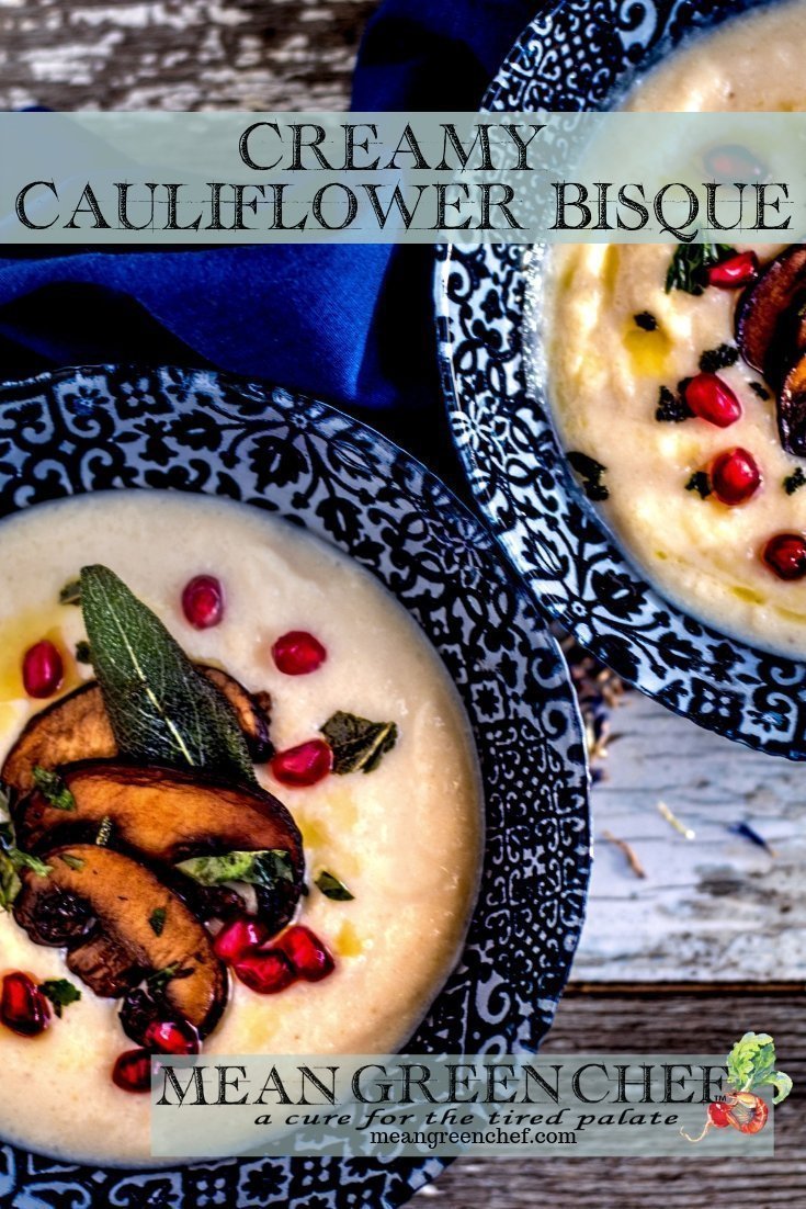 Creamy Cauliflower Bisque ladled into two blue bowls and garnished with smoked portobello mushrooms, fried sage, and pomegranate seeds.