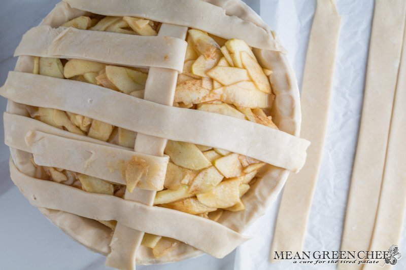 Overhead photo of Lattice Pie Crust being created over a caramel apple pie, photographed on a parchment paper background. Mean Green Chef
