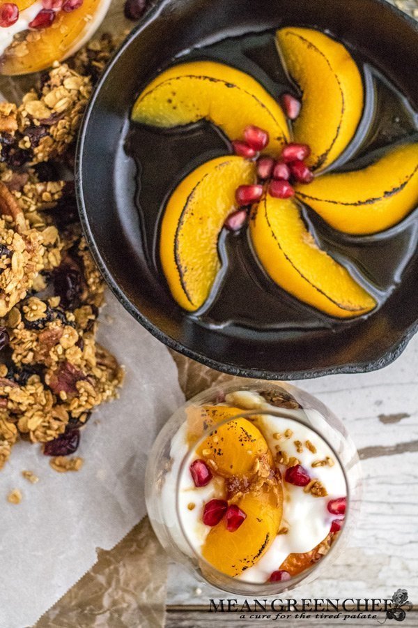 Overhead photo of Easy Peach Parfait with Brown Butter Granola, Roasted Pecans, and Cranberries in a short, stout glass. With a small cast iron pan int he upper right hand corner showing off browned peaches. Mean Green Chef