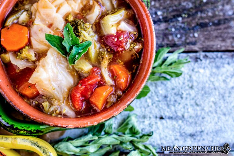 Overhead photo of Robust Cabbage Soup in two crocks one yellow one green with oregano on an old blue wooden background. Mean Green Chef