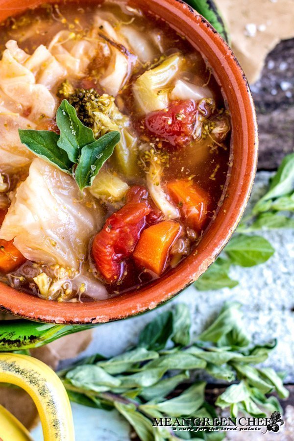 Overhead photo of Robust Cabbage Soup in two crocks one yellow one green with oregano on an old blue wooden background. Mean Green Chef