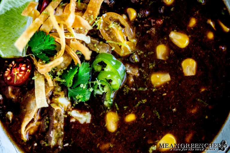 Close up of a bowl of Black Bean Soup garnished with crispy tortilla strips, jalapenos and cilantro.