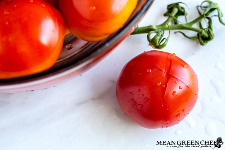 Red ripe tomato with an X scored into the bottom of it for blanching.