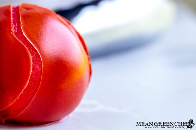 Red blanched tomato with peeling skin on white marbled counter top.